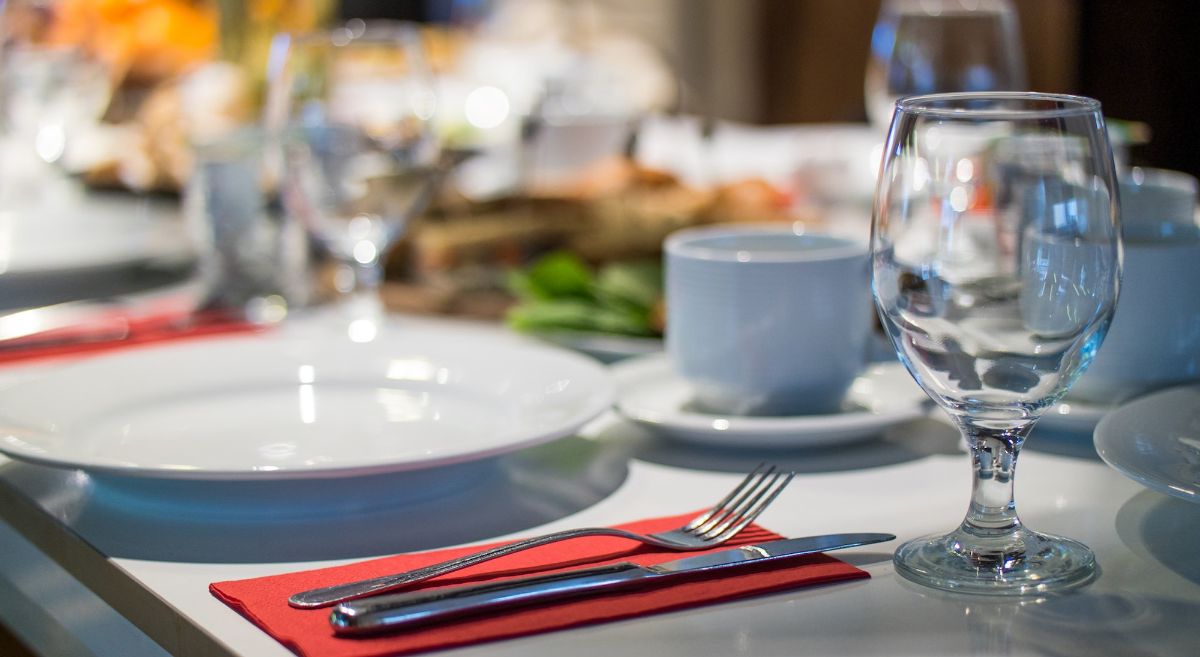 Dining table set with glasses, plates, cutlery and cups